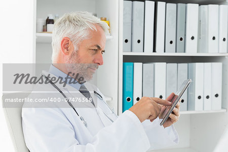 Side view of a concentrated male doctor using digital tablet at medical office