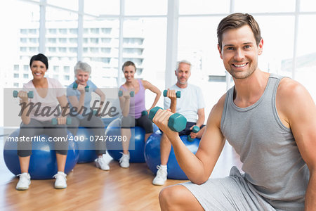 Portrait of fitness class with dumbbells sitting on exercise balls in a bright gym