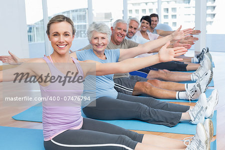 Happy female trainer with class stretching hands at yoga class