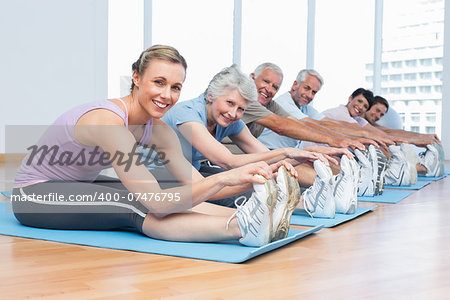 Happy female trainer with class stretching hands to legs at yoga class