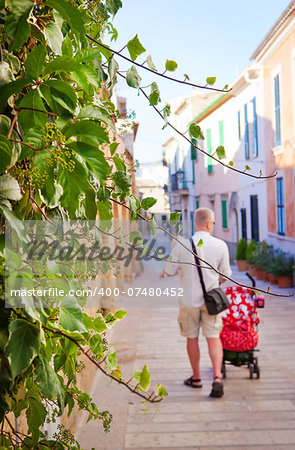 Young man with  baby and stroller walking down a narrow street, Majorca island
