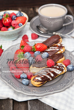 Chocolate eclairs and fresh berries on plate with cup of coffee on the background