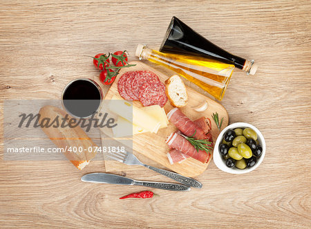 Red wine with cheese, olives, tomatoes, prosciutto, bread and spices. Over wooden table background. View from above with copy space