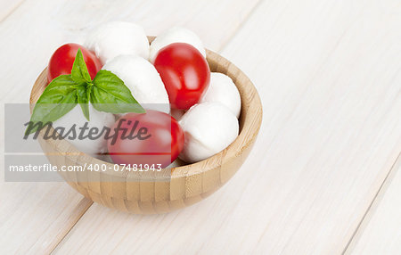 Mozzarella cheese with cherry tomatoes and basil on white wood table