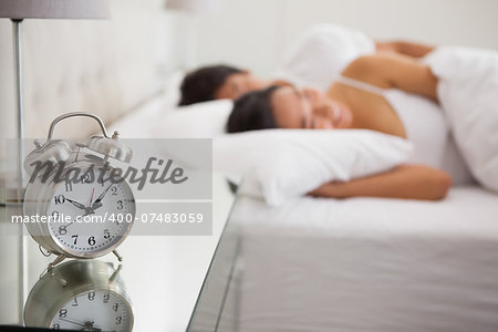 Couple lying in bed with focus on alarm clock at home in bedroom