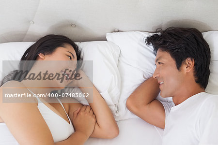 Happy couple lying in bed chatting at home in bedroom
