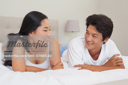 Happy couple lying on bed together at home in bedroom