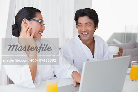 Couple in bathrobes spending the morning together using laptop at home in the living room