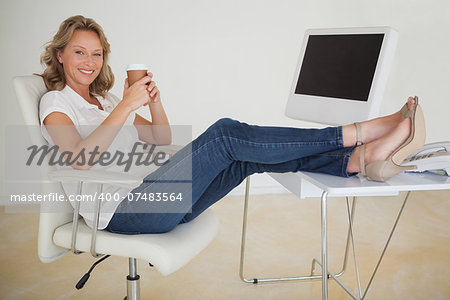 Casual businesswoman having a coffee with her feet up at desk in her office