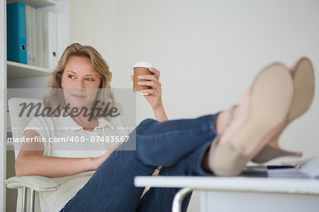 Casual businesswoman having a coffee with her feet up at desk in her office