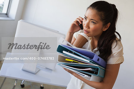 Casual businesswoman balancing coffee on pile of folders in her office