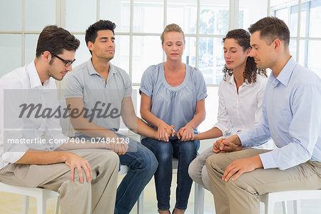 Group therapy in session sitting in a circle holding hands in a bright room