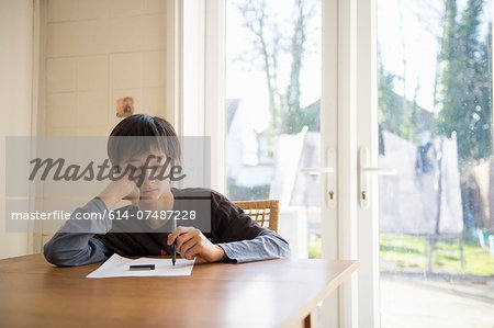 Boy sitting at table, holding pen to paper