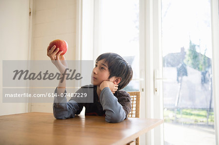 Boy sitting at table, holding an apple in front of him