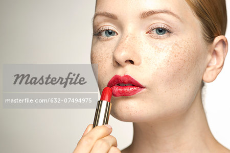 Young woman applying lipstick, portrait