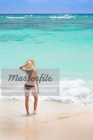 Caribbean, Dominican Republic, La Altagracia province, Punta Cana, Bavaro, Beautiful young woman shot from behind wearing a beach hat and a bikini on the beach facing a turquoise Atlantic (MR)