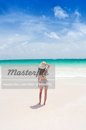 Caribbean, Dominican Republic, La Altagracia province, Punta Cana, Bavaro, Beautiful young woman shot from behind wearing a beach hat and a bikini on the beach facing a turquoise Atlantic (MR)