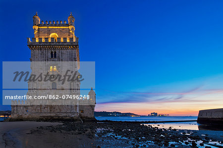 The early 16th century Portuguese Manueline Style, Torre de Belem designed by the architect Francisco de Arruda at twilight with the River Tagus Estuary in the background, in Pedroucos, Belem, Cruz Quebrada, Lisbon, Portugal.