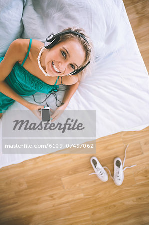 Overhead view of gorgeous smiling blonde listening to music in bright bedroom