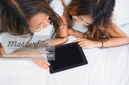 Two cute sisters using a tablet while lying on a bed