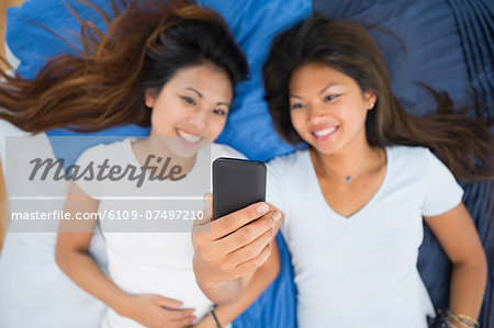 Two pretty sisters taking a picture of themselves while lying on a bed