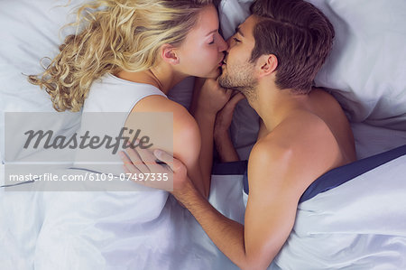 Cute young couple kissing each other while lying in their bed