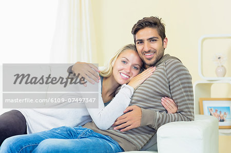Sweet young couple sitting on a couch smiling at the camera