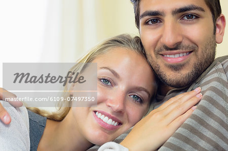 Nice young couple cuddling on couch smiling at the camera