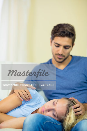 Sad young woman lying her head on the lap of her boyfriend in the living room