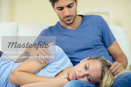 Unhappy young woman lying on the couch having her head on the lap of her boyfriend