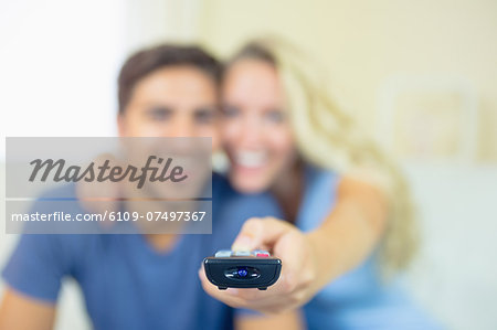 Smiling young couple watching television in the living room using the remote