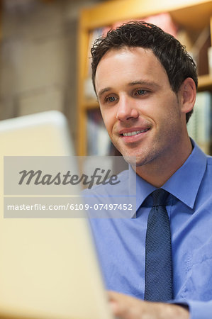 Smiling librarian working at laptop in library in a college