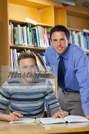 Smiling lecturer and student looking at camera in library in a college