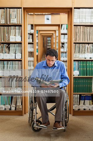 Attractive man in wheelchair reading a book in library in a college