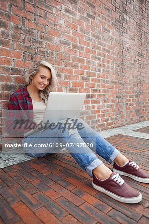 Lucky gorgeous student leaning against wall using laptop on college campus