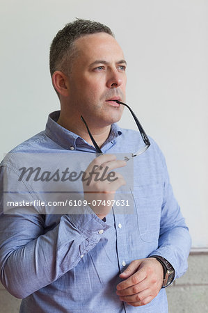 Thoughtful lecturer standing in his classroom biting his glasses in college