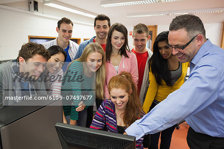 Happy students standing at computer with their lecturer in the computer room in college
