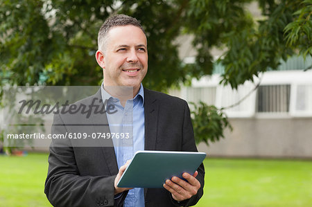 Smiling lecturer using his tablet pc outside on campus at the university