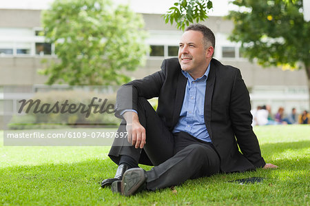 Happy lecturer sitting outside on campus looking away at the university