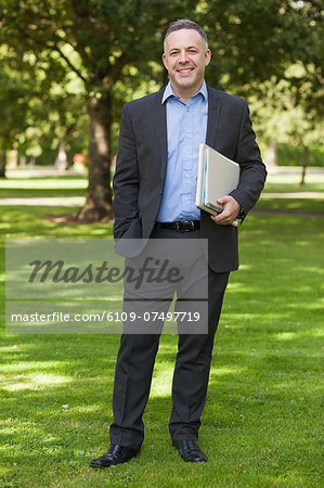 Smiling professor standing on campus holding notepads at the university