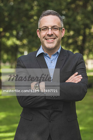 Happy professor looking at camera with arms crossed on campus at the university