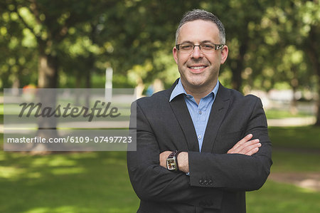 Happy professor looking at camera with arms folded on campusat the university