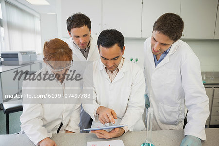 Young male scientist showing his tablet to his colleagues standing in the laboratory