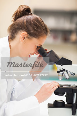 Cheerful brunette student looking through microscope in lab at college