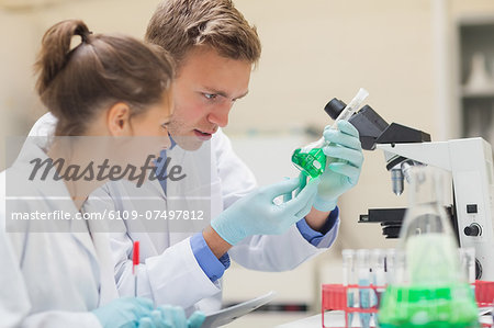 Two focused students looking through microscope and taking notes in lab at college