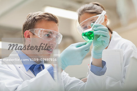 Two students looking at green liquid and taking notes in lab at college