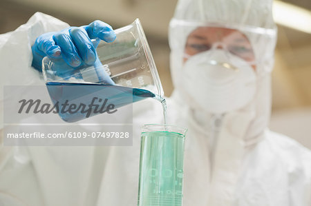 Lab assistant with mask mixing blue liquid in beaker in lab at college Lab assistant with mask mixing blue liquid in beaker in lab at college