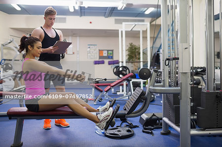 Instructor taking notes of woman exercising in weights room of gym