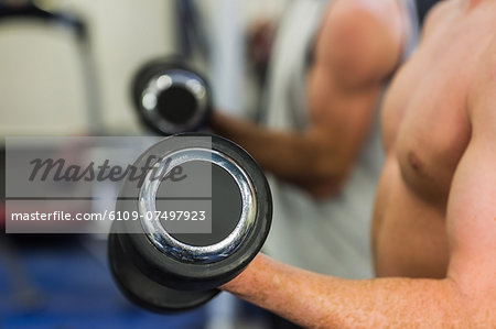 Two muscular men lifting dumbbells in weights room of gym