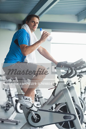 Side view portrait of a tired young man with water bottle working out at spinning class in gym